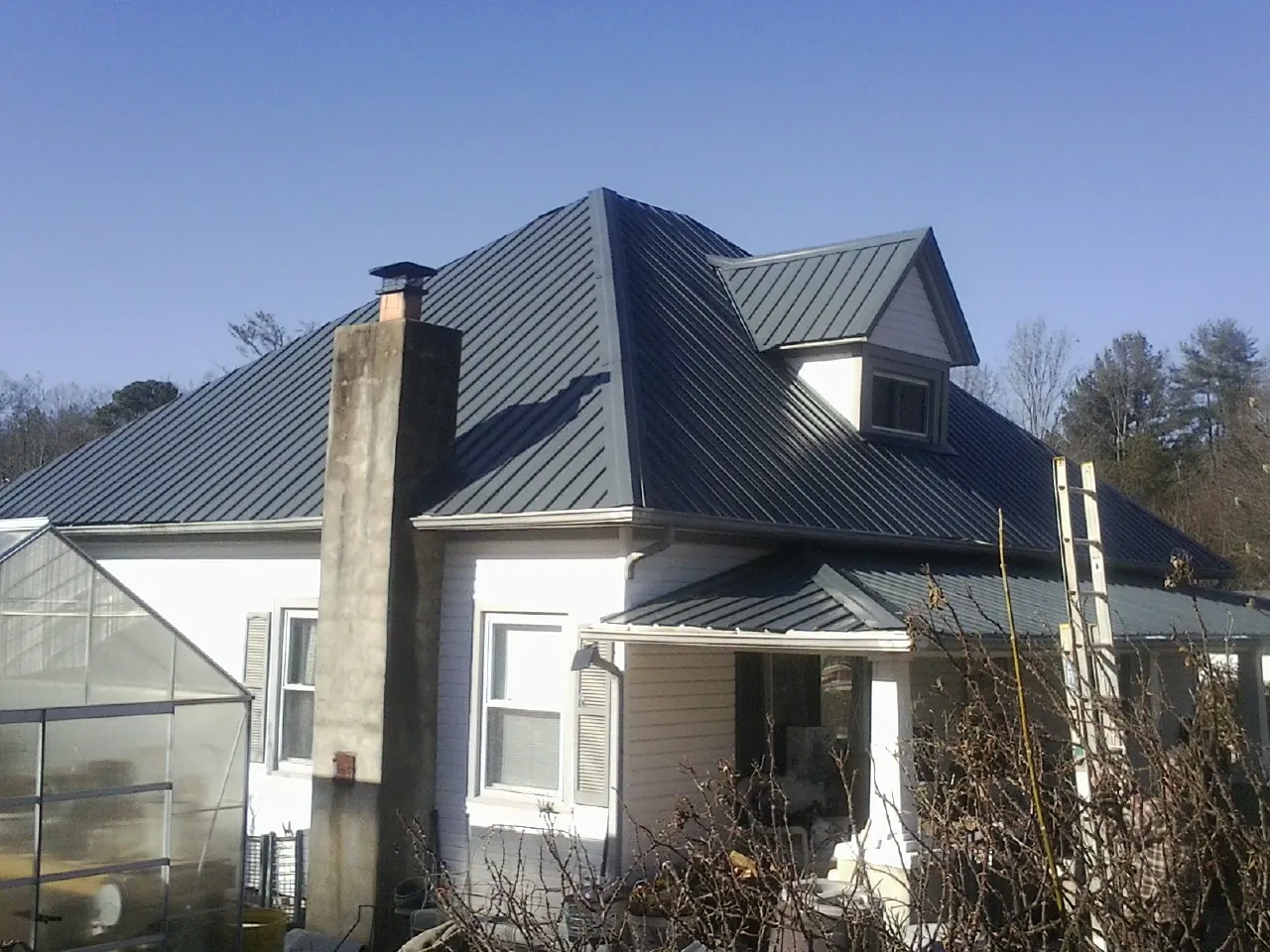 Dark blue standing seam metal roof on a white farmhouse with dormer — Slate & Tile Roof Repair by Roofing Brothers in Rapid City