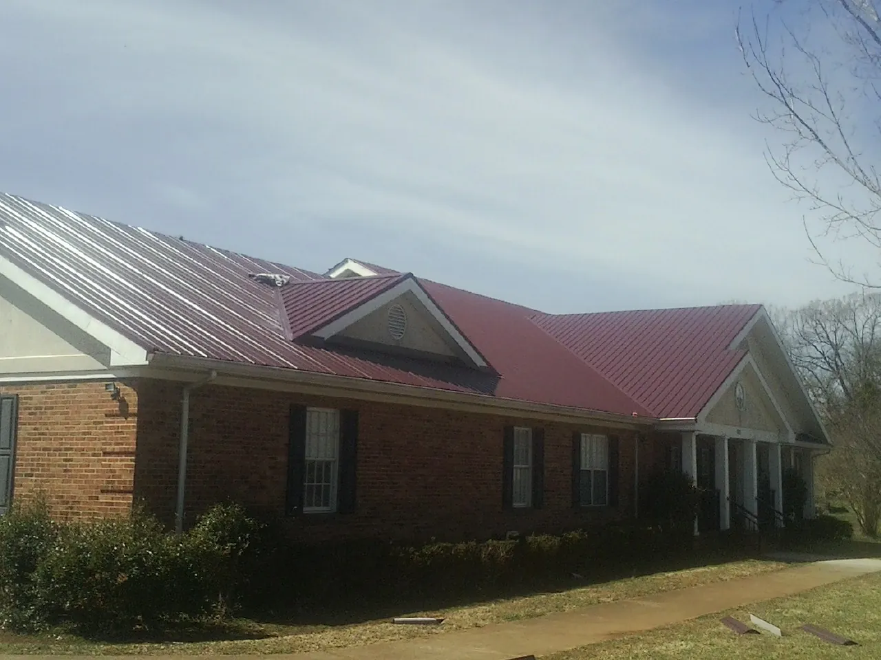 Red metal roof with gabled entries on a long brick building, from a Hail Damage Roof Repair job in Rapid City