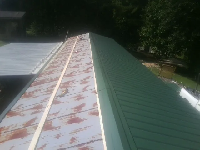 Old rusted panels beside newly installed green metal roofing — Wind Damage Roof Repair by Roofing Brothers in Rapid City